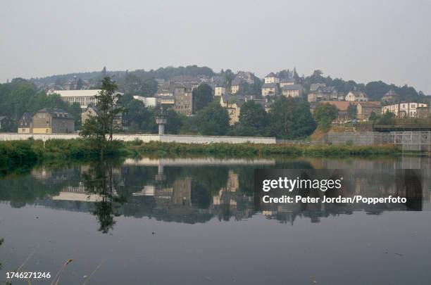 View from West Germany over the River Saale to a concrete wall, fence and East German observation tower in the town of Hirschberg at the border,...