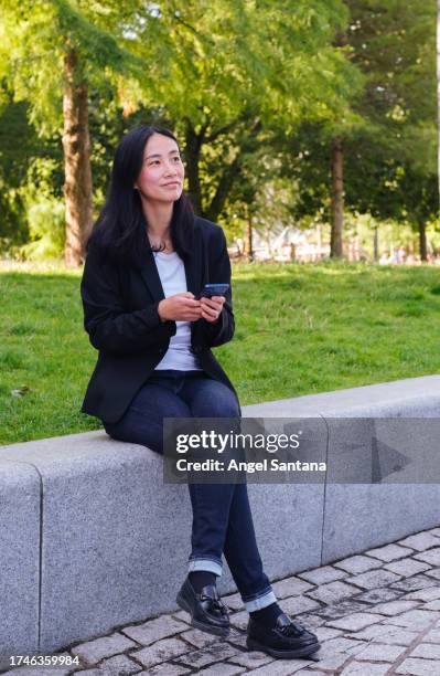woman sits with her mobile, gazing at something ahead - ahead stock pictures, royalty-free photos & images