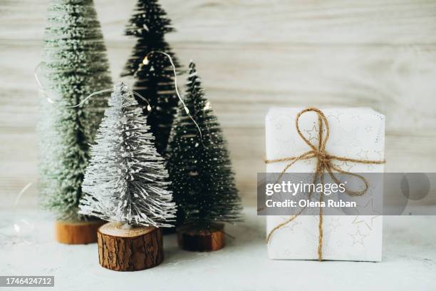 white gift box with string knot against toy snowy christmas trees with led lights on stumps. - led stumps stock pictures, royalty-free photos & images