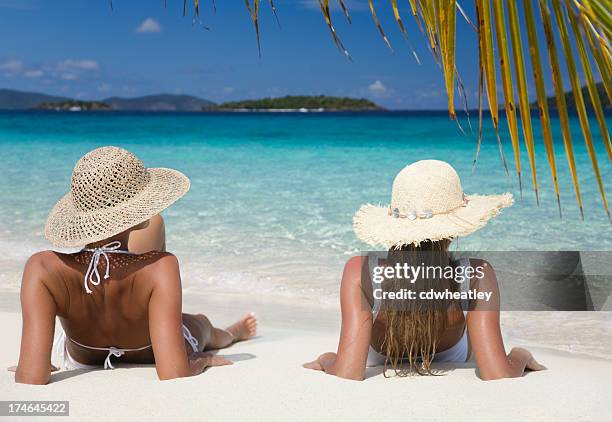 two women relaxing on beautiful tropical beach - blue white summer hat background stock pictures, royalty-free photos & images