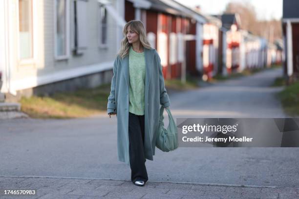 Carmen Kroll seen wearing a pastel light green knit pullover, pastel green wool long coat, black wide leg pants, pastel green leather bag and...
