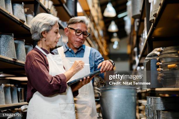 enhanced customer experience with an order management system in your small business operations. proud of small business owners using a tablet computer to check and confirm orders in their warehouse. small business ownership with technology. - pequeña empresa fotografías e imágenes de stock