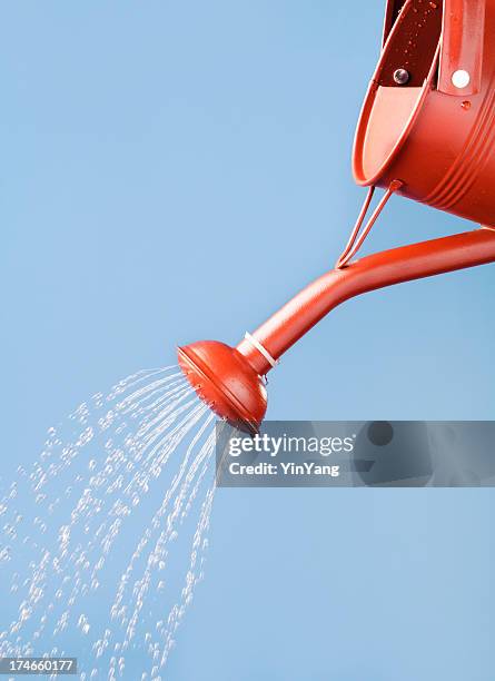 red watering can pouring, sprinkling, flowing water against blue sky - watering can stock pictures, royalty-free photos & images