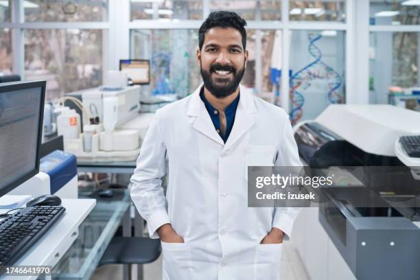 retrato de un joven bioquímico sonriente de pie con las manos en los bolsillos en el laboratorio - bata de laboratorio fotografías e imágenes de stock