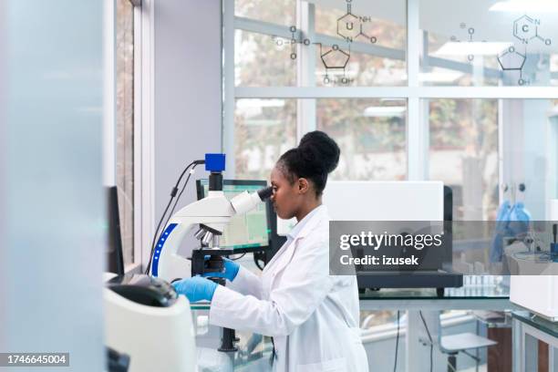 side view of young female scientist looking through microscope at laboratory - scientific sample stock pictures, royalty-free photos & images