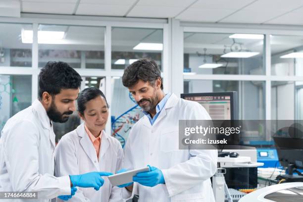 team of biochemists discussing over digital tablet at laboratory - young man scientist stock pictures, royalty-free photos & images