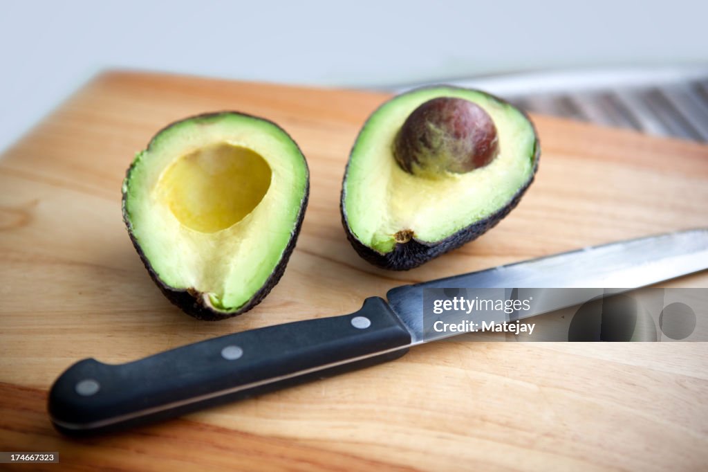 Big knife sitting next to avocado sliced in half