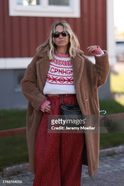 Karin Teigl seen wearing a brown sunglasses, Copenhagen Studios white / red logo pattern knit wool pullover, brown fluffy long teddy coat, red print...