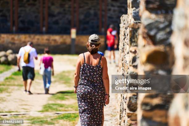 rear view of a tourist woman in a dress walking on the grass of the courtyard of an ancient castle on a sunny day - sunny leon stockfoto's en -beelden