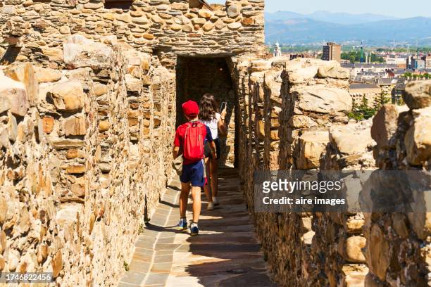 rear view of two boys in casual clothes and backpack walking on the wall of ponferrada castle - ponferrada ストックフォトと画像