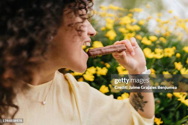 woman in profile biting chocolate bar on spring day - chocolate bar stock pictures, royalty-free photos & images