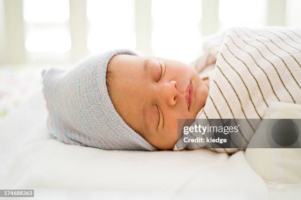 new-born baby sleeping on a bed wearing a blue hat - baby blanket stock pictures, royalty-free photos & images
