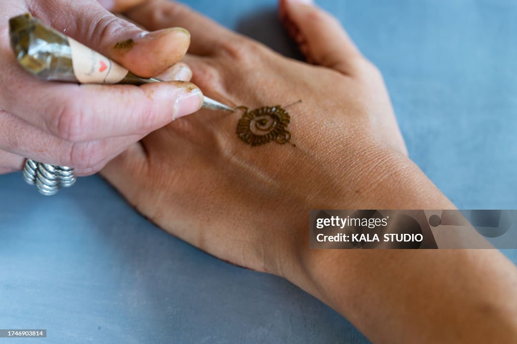 Tattoo artist drawing lines with henna in a hand