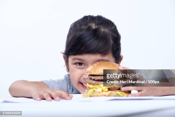 portrait of girl eating burger against white background - heri mardinal stock pictures, royalty-free photos & images