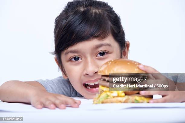 close-up of girl having burger against white background - heri mardinal stock pictures, royalty-free photos & images