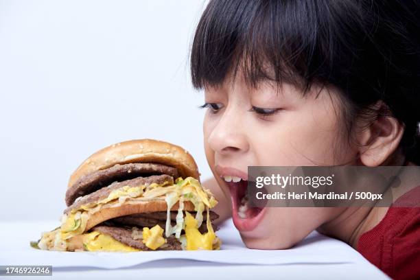 close-up of girl eating burger against white background - heri mardinal stock pictures, royalty-free photos & images