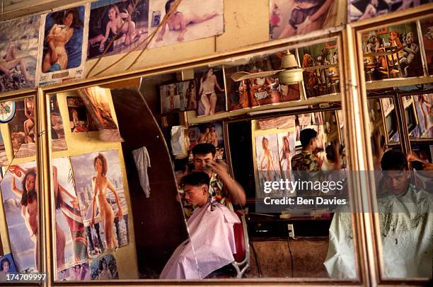 Traditional village barber shop in remote Tha Li district where villagers are entertained by posters of semi-naked girls whilst they have their hair...