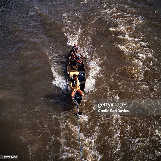 Small dug out canoe is pulled behind one of the passenger steamers sailing up the Amazon River near Manaus in the lush rain forest of Brazil. The...