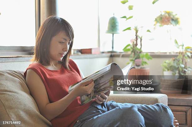 woman reading a magazine while sitting on a couch - sleeveless stock pictures, royalty-free photos & images