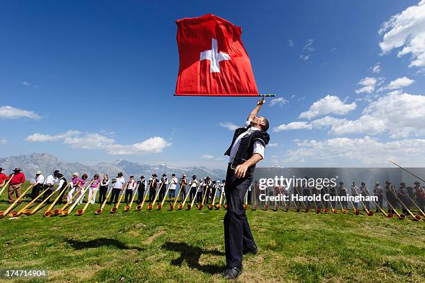 Man throws a Swiss flag as alphorn players perform on July 28, 2013 in Nendaz, Switzerland. About 150 alphorn blowers performed together on the last...