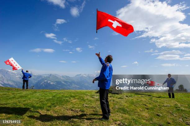 Men throw a Swiss and canton of Valais flags on July 28, 2013 in Nendaz, Switzerland. About 150 Alphorn blowers performed together on the last day of...