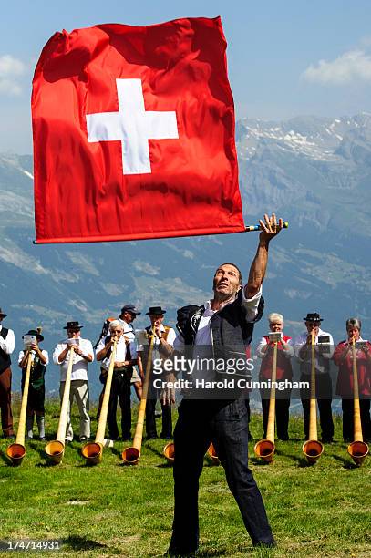 Man throws a Swiss flag as alphorn players perform on July 28, 2013 in Nendaz, Switzerland. About 150 alphorn blowers performed together on the last...