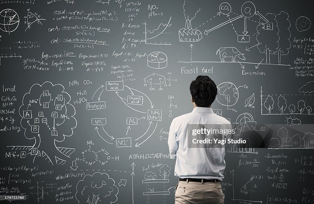 Man looking to formula and picture on blackboard