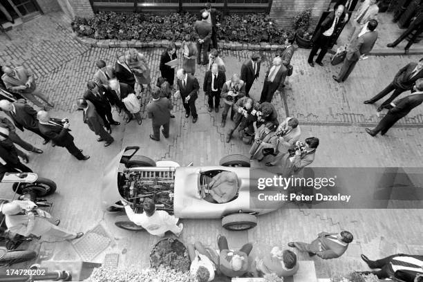 Argentinian racing car driver Juan Manuel Fangio poses for photographers in a 1954 Mercedes-Benz W196R at the Porter Tun Rooms, Chiswell Street,...