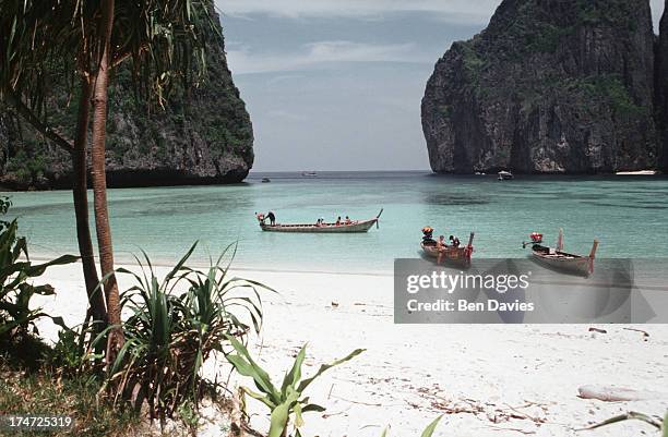 Fishing boats drawn up on the white sparkling beaches of Maya Bay, Ko Phi Phi in Southern Thailand. Turquoise seas and sandy beaches have made the...