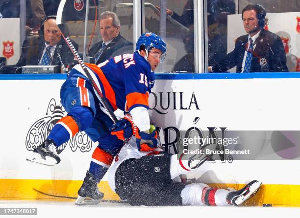 Cal Clutterbuck of the New York Islanders hits Nico Hischier of the New Jersey Devils into the boards during the first period at UBS Arena on October...