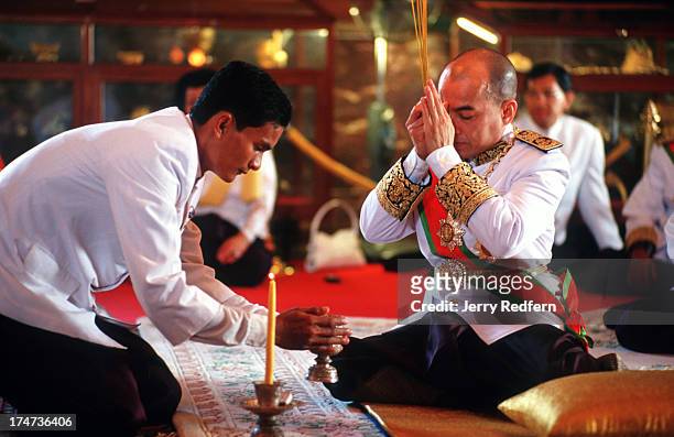 With the help from an attendant, King Norodom Sihamoni lights candles and incense and prays for his ancestors at a ceremony in the Silver Pagoda of...