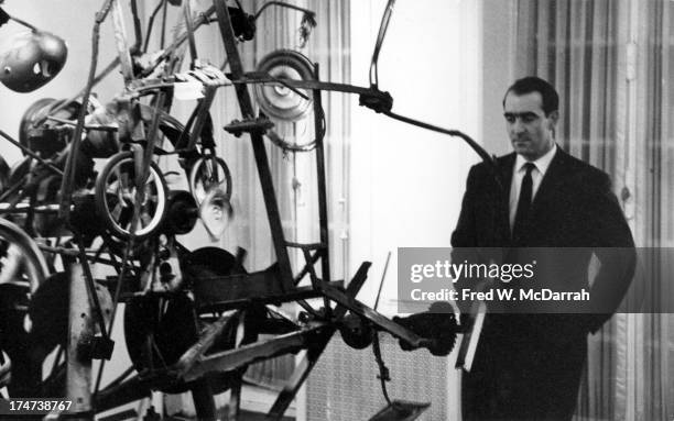 Portrait of Swiss painter and sculptor Jean Tinguely as he poses in front of one of his works at the Alexander Iolas Gallery, New York, New York,...