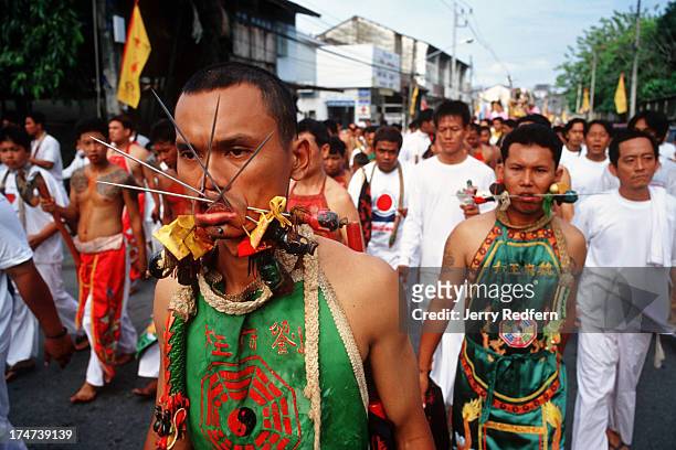 Young men channelling spirits walk the streets of Phuket with their cheeks pierced with skewers to ward off evil from the community in the coming...