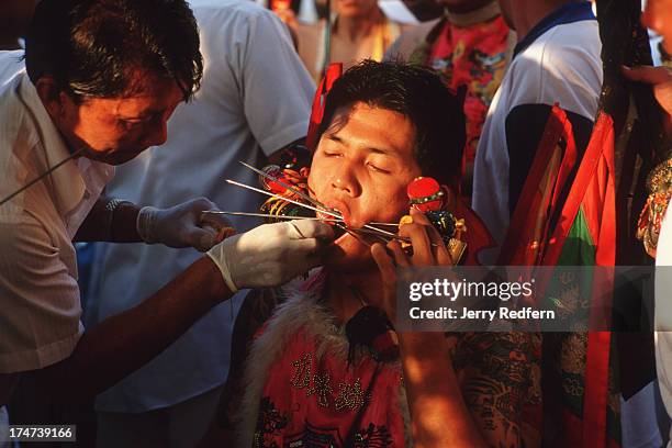 Young man channelling a spirit has his cheeks pierced with skewers to ward off evil from his community in the coming year at the Phuket Vegetarian...