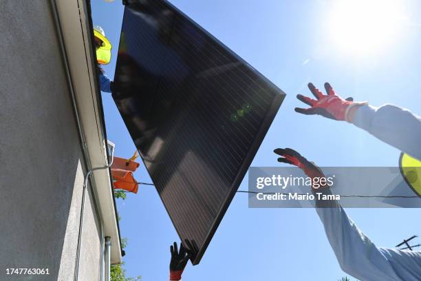 Alternatives employees hoist a solar panel as they install no-cost solar panels on the rooftop of a low-income household on October 19, 2023 in...
