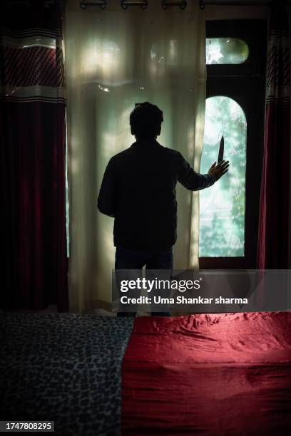 silhouette of a murderer holding a knife and standing against curtains in bedroom. - murder victim stock pictures, royalty-free photos & images