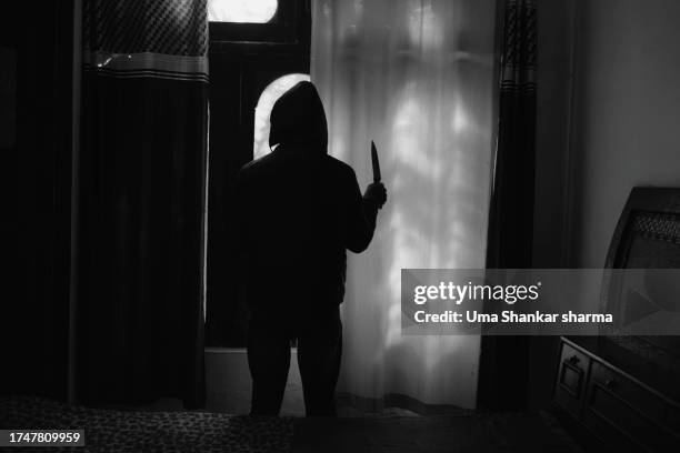 silhouette of a murderer in hoodie holding a knife and standing against curtains in bedroom - murder victim stock pictures, royalty-free photos & images