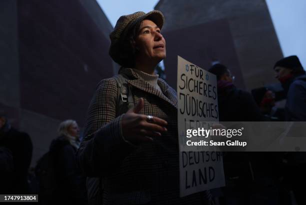 Participant holds a sign reading "For safe Jewish life in Germany" as she speaks to a television reporter during a vigil outside the community center...