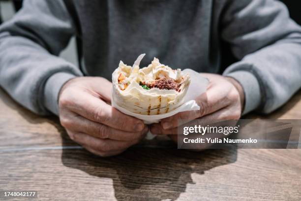 an adult man eating shawarma. hands close-up. - halal stock pictures, royalty-free photos & images