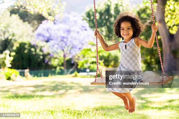 lächelnd junges mädchen auf einer schaukel in einem park - mädchen kleid stock-fotos und bilder