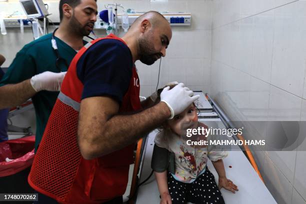 Palestinian nurse Mahmud al-Astal attends to a little girl with a head wound as she sits on an examining table at the Nasser hospital following...