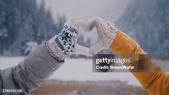 Two women making heart sign gesture in knitted woolen winter gloves on cold winter day