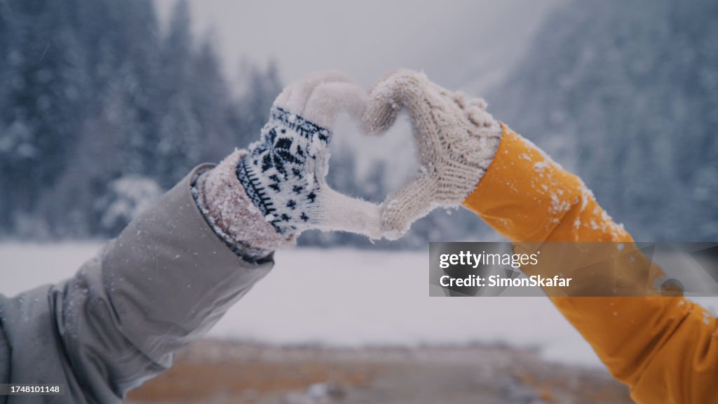 Two women making heart sign gesture in knitted woolen winter gloves on cold winter day