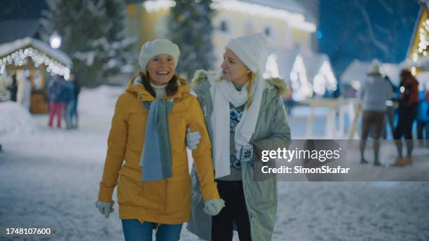 two women in warm clothing at christmas decorated street during night - kranjska gora stock pictures, royalty-free photos & images
