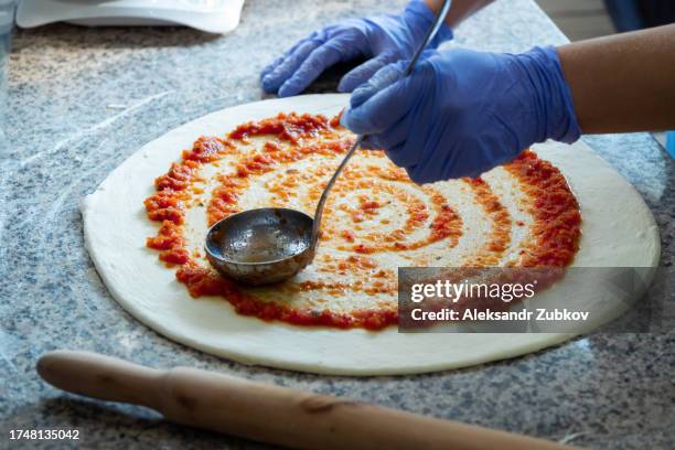 cooking italian vegetarian pizza at home, in a pizzeria or cafe. a woman, a baker, a chef, a pizza maker spreads ketchup or tomato paste on rolled dough with a spoon. the concept of food. step-by-step instructions, do it yourself. a simple life. - georgia country stock pictures, royalty-free photos & images