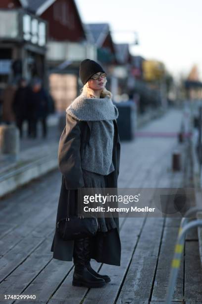 Katarina Krebs seen wearing a black wool knit beanie, black sunglasses, grey wool knit round loop scarf, grey wool knit pullover, grey long wool...