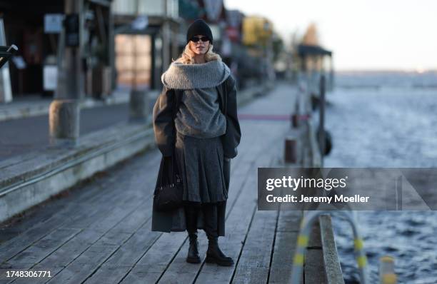 Katarina Krebs seen wearing a black wool knit beanie, black sunglasses, grey wool knit round loop scarf, grey wool knit pullover, grey long wool...