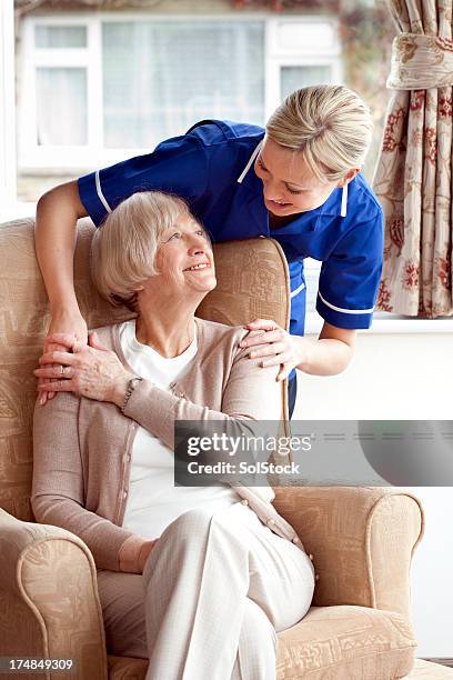 junge pflegekraft lächeln in älteren lady - pflegedienst blau stock-fotos und bilder