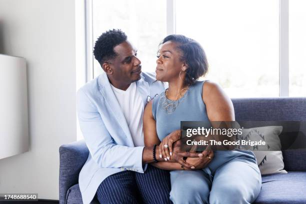 portrait of loving mature couple sitting on sofa by window - business mature couple portrait stock pictures, royalty-free photos & images