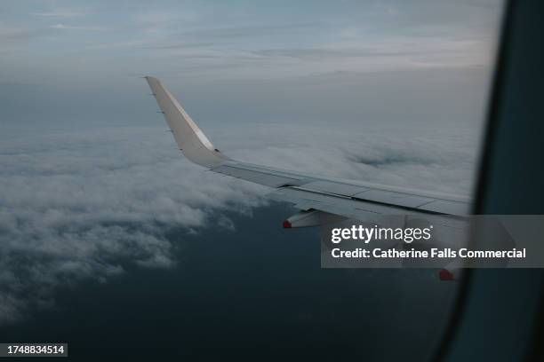 wing of an airplane mid air, flying above clouds and ocean at dusk - airport tarmac stock pictures, royalty-free photos & images
